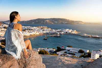 Woman sitting on rock while looking at sea against sky