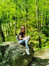 Portrait of smiling young woman sitting on rock in forest