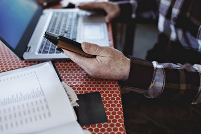 Midsection of retired senior man paying bills through credit card while using technologies at dining table