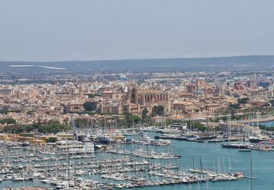 Sailboats moored in harbor by buildings against sky