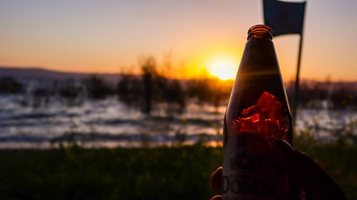 Close-up of bottle on field against sky during sunset