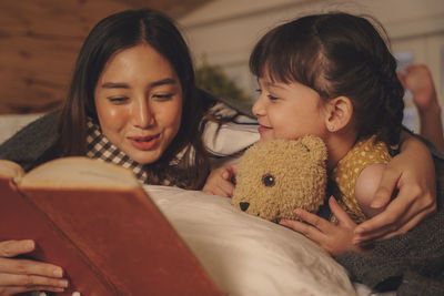 Mother and girl reading book while relaxing on bed