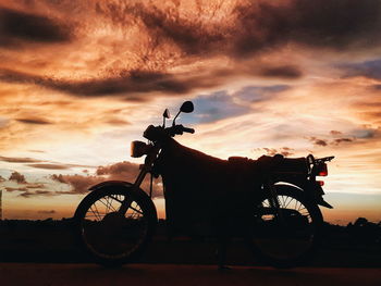 Bicycle on street against dramatic sky during sunset