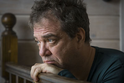 Mature man looking away while leaning on wooden railing at home