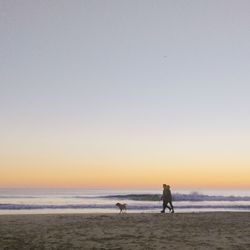 People on beach against clear sky during sunset