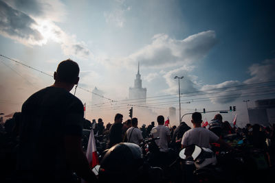 Rear view of people in city against cloudy sky