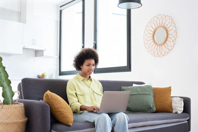 Young woman using laptop while sitting on sofa at home
