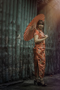 Young woman in traditional clothing holding umbrella by old shutter
