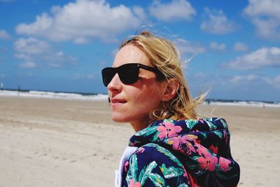 Young woman wearing sunglasses on beach against sky