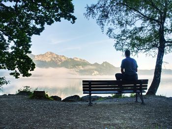 Man sit lone on a bench in park next lake. mountain range with amazing view over smooth lake