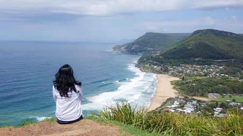 Rear view of woman sitting on cliff against beach