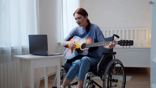Young woman playing guitar while sitting on wheelchair
