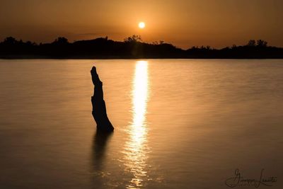 Silhouette person on lake against sky during sunset
