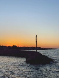 Lighthouse by sea against sky during sunset