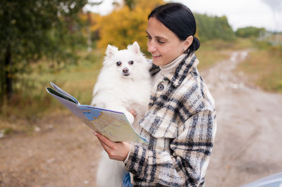 A cute girl holds a white pomeranian and a travel roadmap in her hands