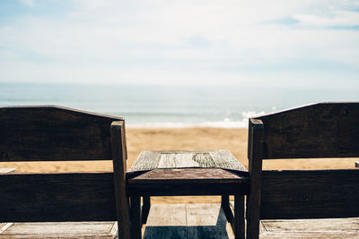 Wooden chair on beach against sky