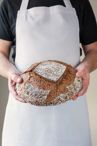 Midsection at bakers hands holding a round shaped loaf of organic sourdough bread in front of him.