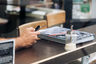 Cropped image of hand using phone at cafe