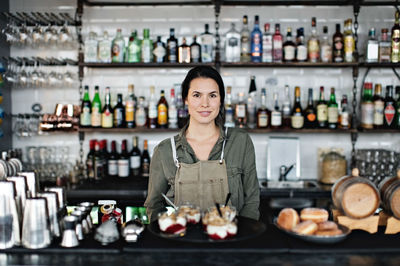 Portrait of confident female owner with dessert standing at counter in restaurant