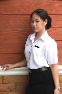 Young woman looking away while standing against wall