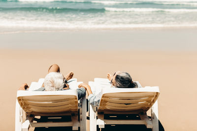 Retired couple resting on a adirondack chair by the beach in the sunlight and clean sandy beach. 