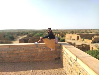 Portrait of man on retaining wall against clear sky