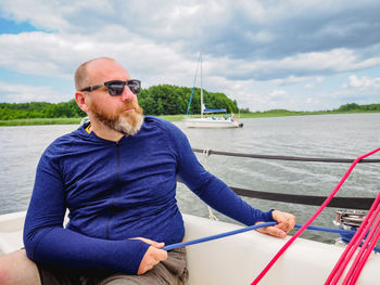 Adult bearded man using a winch to pull a blue rope on a sailboat or sailing yacht