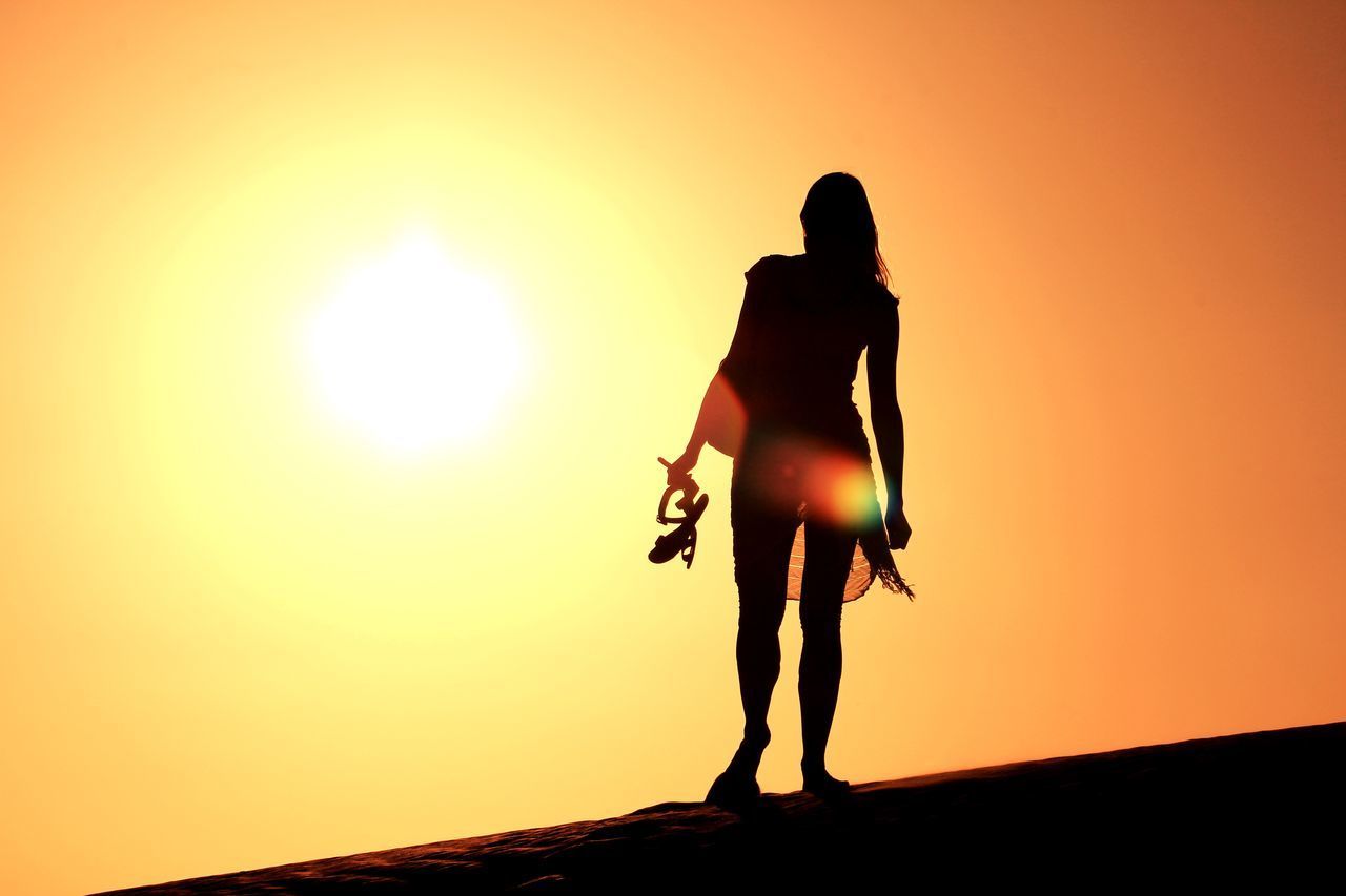 Low angle view of silhouette woman standing on sand dune during sunset