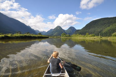 Rear view of woman on canoe on lake against mountain range