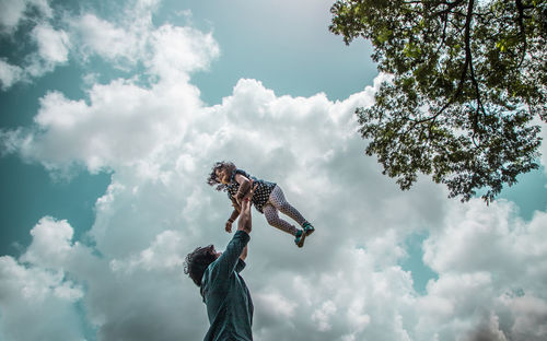 Low angle view of man playing with a child in air against sky