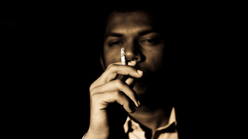 Close-up of young man holding cigarette against black background