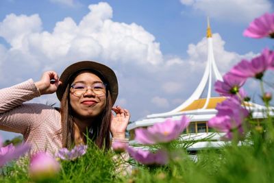 Portrait of woman with pink flowers against sky