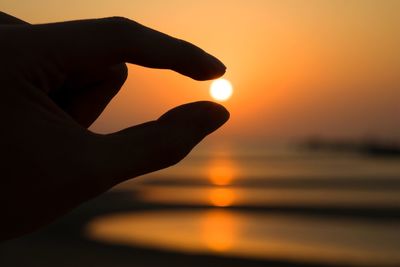 Optical illusion of silhouette hand holding sun against sky during sunset
