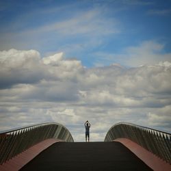 People walking on railing against cloudy sky