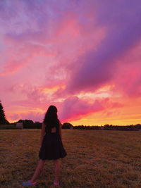 Woman standing on field against sky during sunset