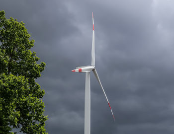 Low angle view of wind turbine against cloudy sky