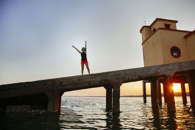 Low angle view of woman exercising on pier over sea against sky during sunset