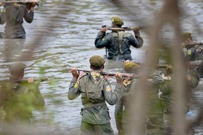 Rear view of male soldiers walking with guns in river
