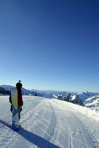 Full length of woman standing on snow covered landscape against clear blue sky