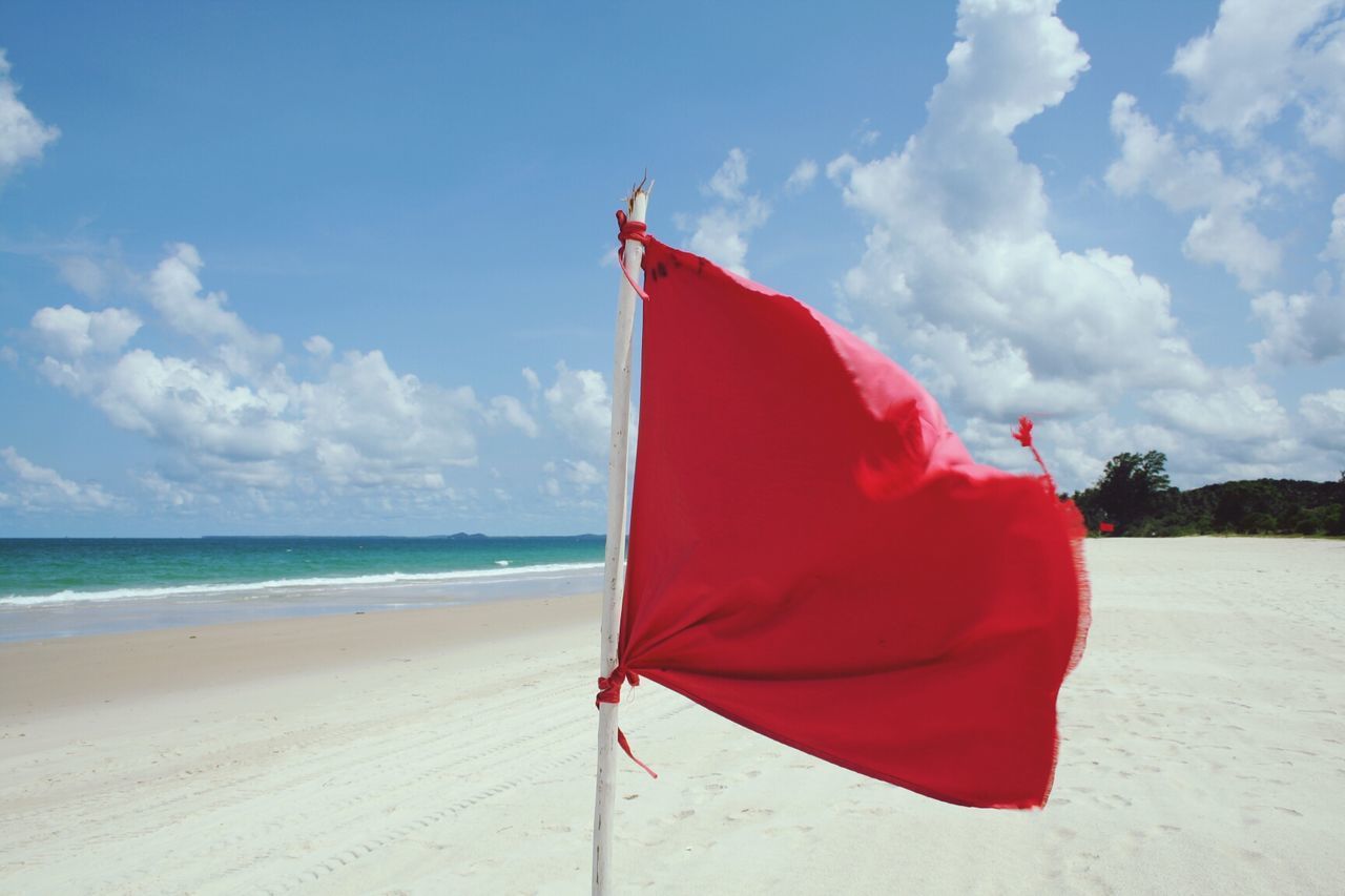 Red flag on calm beach against blue sky