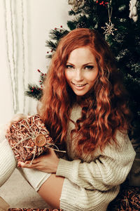 Portrait of smiling young woman sitting by christmas tree