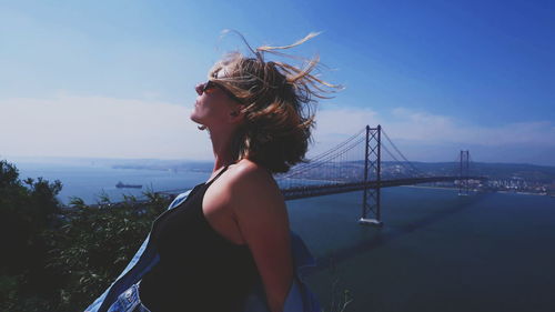 Young woman standing by bridge against sky