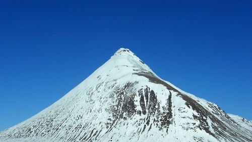 Low angle view of snow covered mountain against blue sky