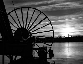 Silhouette ferris wheel by lake against sky during sunset