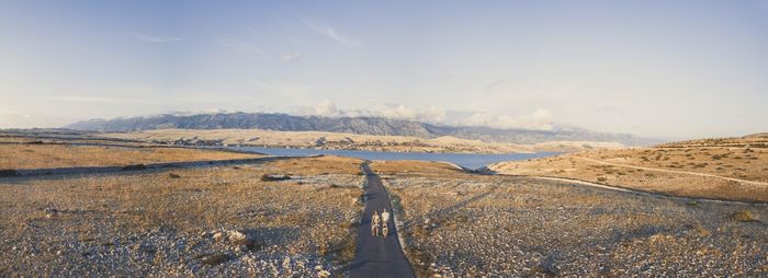 People walking on road by land against sky