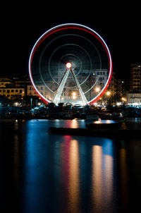 Illuminated ferris wheel by lake in city at night