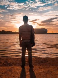 Rear view of man standing at beach against sky during sunset