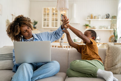 Nervous african american mother ignoring playful little boy son while working remotely on laptop