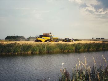 Yellow cart on field by lake against sky