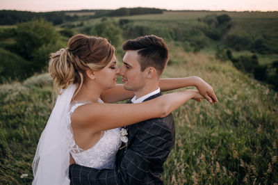 Side view of newlywed couple rubbing noses on grassy field